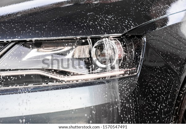 Water drops and foam on the car light in the\
vehcle wash station. Cleaning automobile concept, underground water\
pollution.