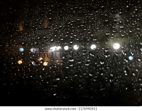 Water drops and\
lights on the glass at\
night.