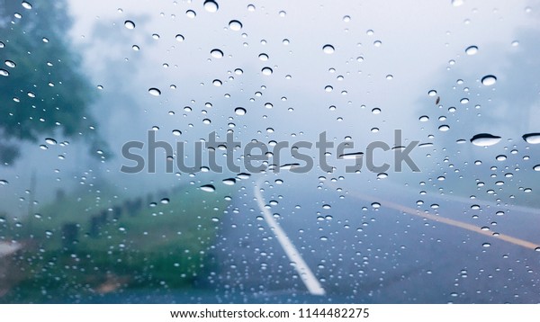 Water drops on car window\
after the rain with blur line street Road and fog background in the\
forest