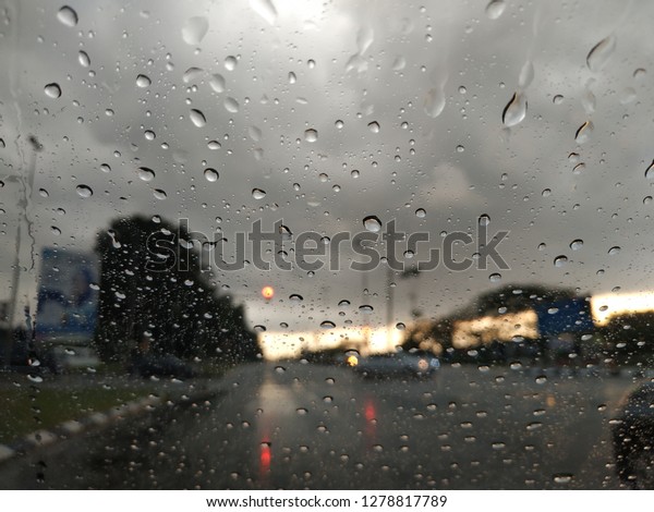 Water drops on car windshield with evening roadside\
under cloudy weather 