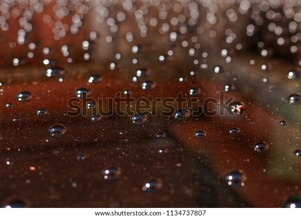 Water drops on top of a car with reflections\
of a building in the\
background.