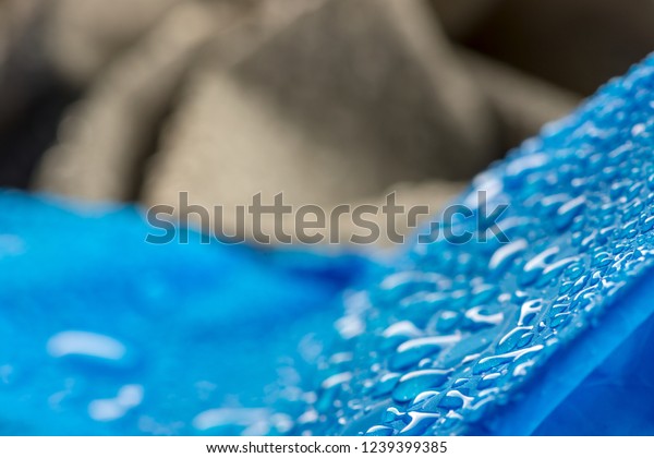 Water drops on\
waterproof blue nylon fabric. Macro detail view of woven synthetic\
waterproof clothing. Heavy blurred background. Rain Drops on Water\
Resistant Textile\
Coating.