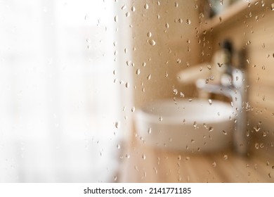 Water Drops On Wet Glass Shower Door In Hotel Bathroom With Blured Bokeh Window, Sink, Faucet And Wooden Furniture On Sunny Morning Or Day. Travel, Holiday, Vacation, Interior Design, Body Care