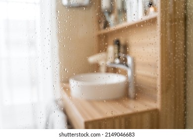 Water Drops On Wet Glass Shower Door In Hotel Bathroom With Blurred Bokeh Window, Sink, Faucet And Wooden Furniture On Sunny Morning Or Day. Travel, Holiday, Vacation, Interior Design, Body Care