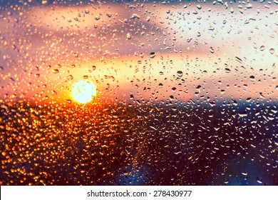 Water Drops On A Window Glass After The Rain. The Sky With Clouds And Sun On Background.