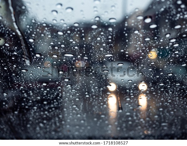 Water drops on windshield with blur car headlight\
on the street in rainy day, view from inside the car. Street view\
in rainy day in rainy\
season.