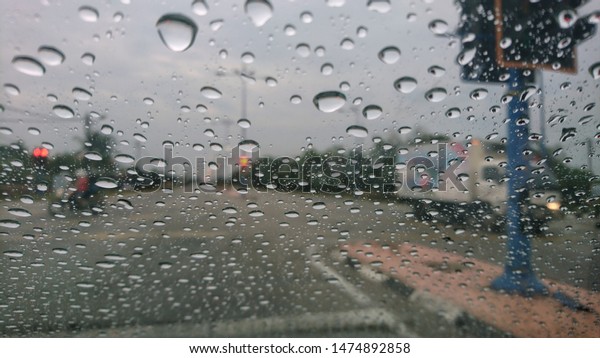 Water drops or rain in front\
of mirror of car on road or street. Driving in rain. Blurred\
background.