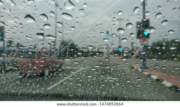 Water drops or rain in front
of mirror of car on road or street. Driving in rain. Blurred
background.