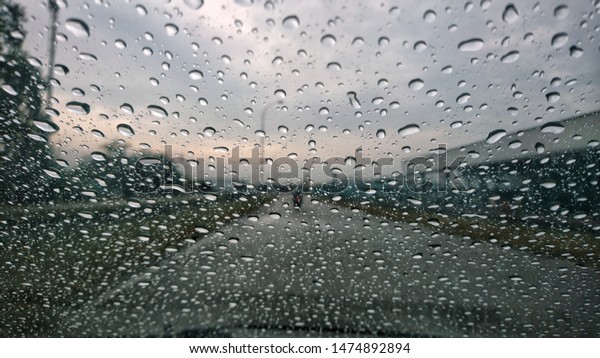 Water drops or rain in front\
of mirror of car on road or street. Driving in rain. Blurred\
background.