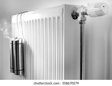 Water Evaporation From Metal Containers On Radiator. Concept Of Good Indoor Climate In Winter Season. Black And White Image