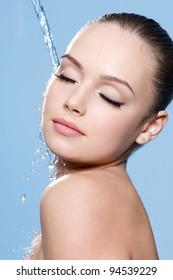 Water falling on the clean beautiful young female face - blue background
