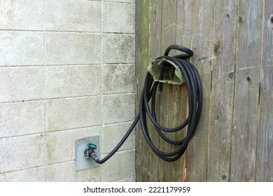 Water Faucet And Coiled Black Garden Hose On Wall