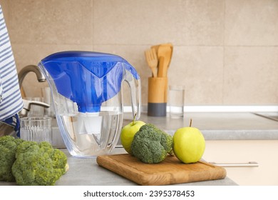 A water filter stands in the kitchen with fresh vegetables - Shutterstock ID 2395378453
