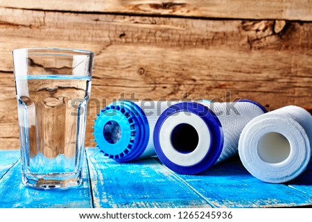 Water filters. Carbon cartridges and a glass of water on a wooden background. Household filtration system.