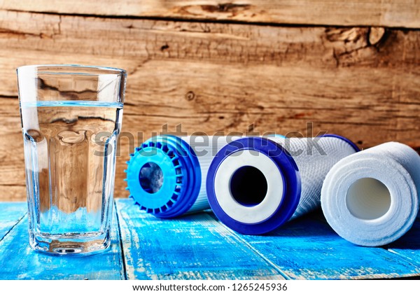 Water filters.\
Carbon cartridges and a glass of water on a wooden background.\
Household filtration\
system.
