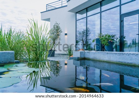 The water in the fish pond reflects the view of the glass wall of the modern home and creates a soothing mood. Out-of-town lifestyle