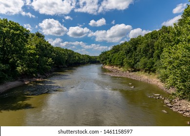 Water Flowing Along Rocky Riverbank  Of Sangamon River Surrounded By Trees On A Sunny Day With Clouds