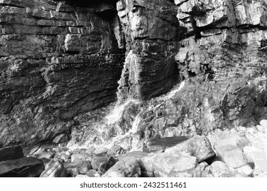 Water flowing from a fissure in the limestone cliff face, after a period of heavy rain, at Pendine, Carmarthenshire, Wales, UK.