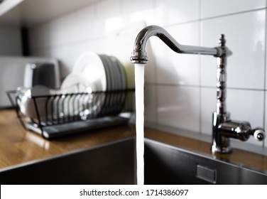 Water flowing out of a kitchen stainless steel tap into the sink. Wasting water by leaving a chrome faucet tap running. Overusing household water. Water misuse in domestic duties and activities.