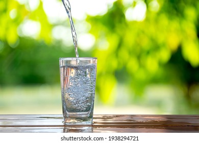 Water flows into a glass placed on a wooden bar. - Shutterstock ID 1938294721