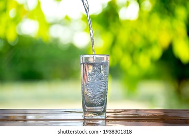 Water flows into a glass placed on a wooden bar.