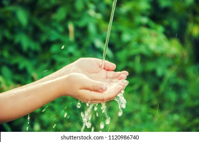 Water flows into the hands of the child. Selective focus.