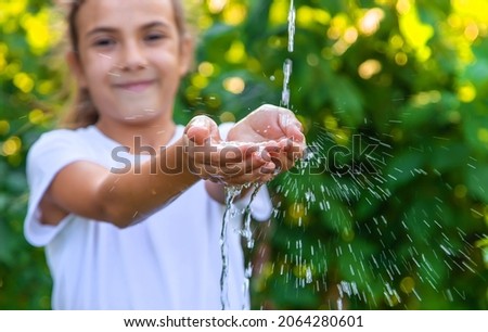 The water flows into the hands of the child. Selective focus. Nature.