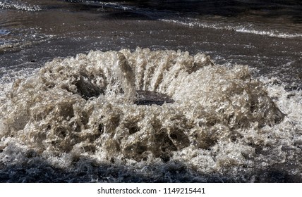 Water flows out of drainage hatch. Drainage fountain of sewage. Accident in sewage system. Dirty sewer water flows fountain on road. Drainage system for wastewater discharge does not work
