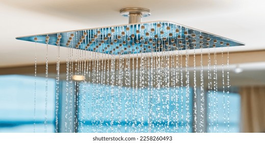 Water flows from the tropical shower. Large water consumption. Chrome large shower head, modern design. Water flowing from the square shower head in a modern bathroom. - Shutterstock ID 2258260493