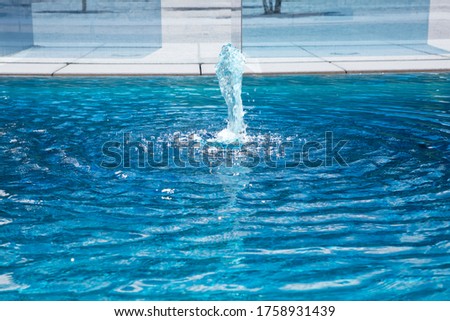 Water fontaine in empty azure shimmering swimming pool