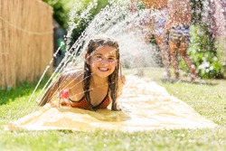 Water Fun In Garden - Girl Cooling Down With Water Sprinkler On Garden Slide