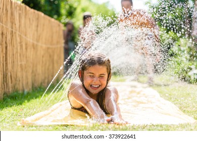 Water Fun In Garden - Girl Cooling Down With Water Sprinkler On Garden Slide