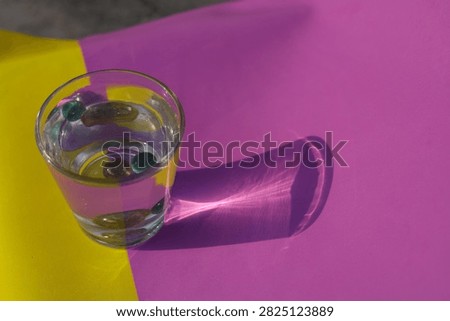 A water glass with marbles casts a sharp caustic light refection pattern on colorful paper under bright outdoor sunlight.