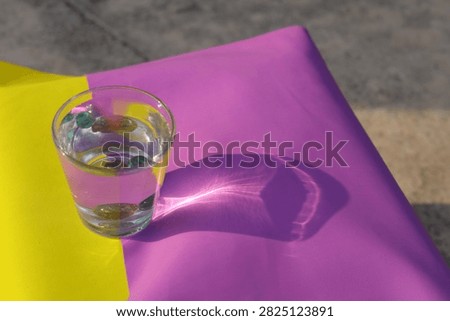 A water glass with marbles casts a sharp caustic light refection pattern on colorful paper under bright outdoor sunlight.