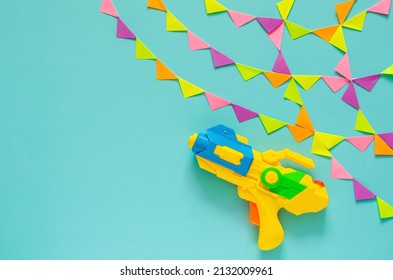 Water gun with colorful party flag for Songkran festival celebration on blue color background. Minimal holiday concept.