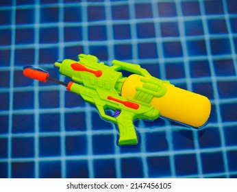 Water Gun. Colorful Squirt Gun In Neon Color Yellow And Green. Water Gun Is Floating In The Swimming Pool.