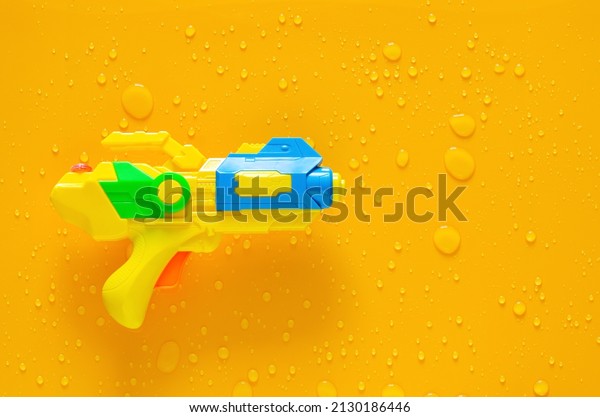 Water gun\
puts on clear mirror that have wet yellow background below for\
Minimal Songkran festival celebration\
concept.