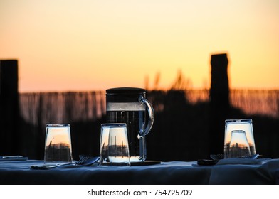 Water Jar And Glasses Upside Down On Table Set Outdoors At Splendid Sunset. Countryside Dinner, Summer Celebration Concepts