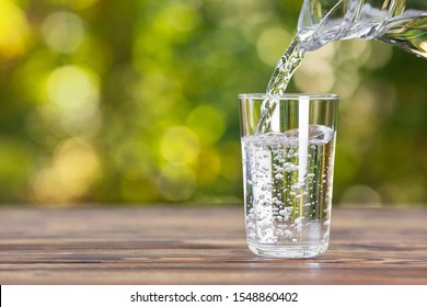 agua de jarra vertida en vidrio sobre mesa de madera al aire libre
