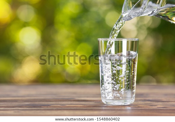water from jug pouring into glass on wooden
table outdoors