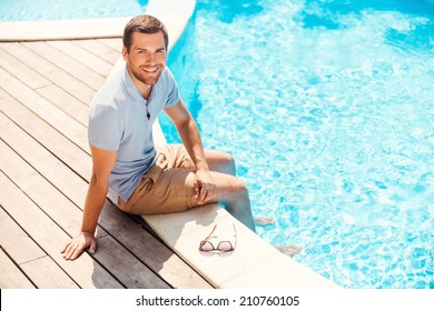 Water Is Just Great! Top View Of Cheerful Young Man In Polo Shirt Sitting By The Pool And Smiling