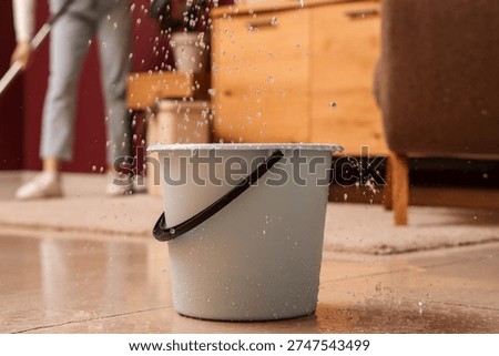 Water leaking from ceiling into grey bucket in living room, closeup. Flood concept