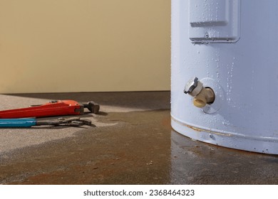 Fugas de agua de un calentador de agua eléctrico residencial con un par de herramientas de plomero.