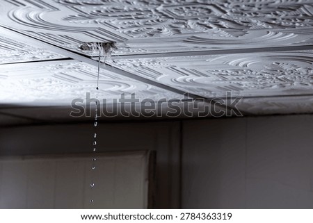 Water leaking through damaged ceiling tile inside house during rainstorm. Ceiling water leak from broken roof or pipe inside residential home