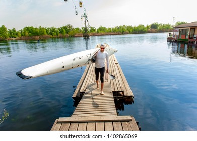 Water leisure in summer. Active young oarsman standing on pier with his equipment, kayak and paddle, after rowing competition - Powered by Shutterstock