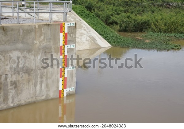 Water level indicator at concrete wall of water\
gate for monitoring support agriculture. Trees and dam background.\
Level indicator, water gate, water management, saving environment\
concept.