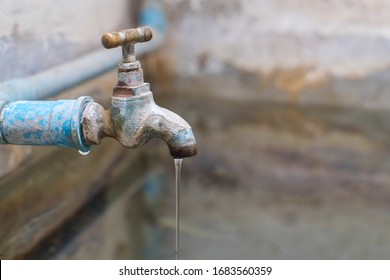 Water from old bass faucet connect to the blue pvc pipe flowing into water surface of bath made of cement close-up.