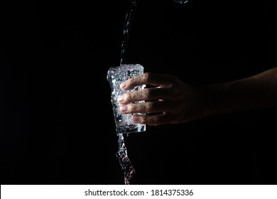 Water on a black background. A glass overflowing with water. Water is poured out of the glass. Pure water