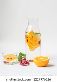 Water With Orange Slices, Pomegranate Seeds And Mint In A Glass Jug On A White Background
