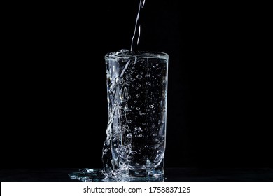 Water overflows the glass. Photo on a black background. Pure and purified water. Water pouring out of a glass